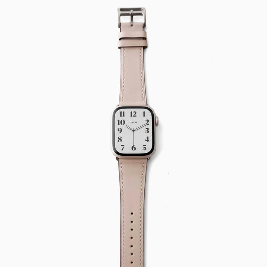 A STARLIGHT BEIGE leather Apple Watch band with a silver buckle and a watch face displaying time and date.