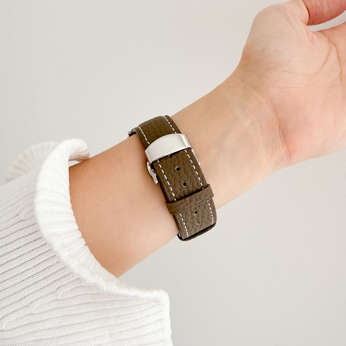 Migliara Apple Watch Band in olive leather worn on wrist with a white knit sleeve, angled view