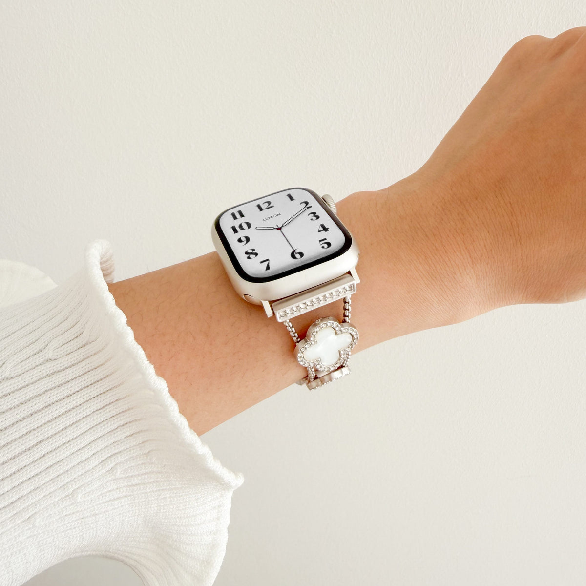 Lucky Clover Apple Watch Bracelet in Starlight worn on wrist with a white knit sleeve, watch face view