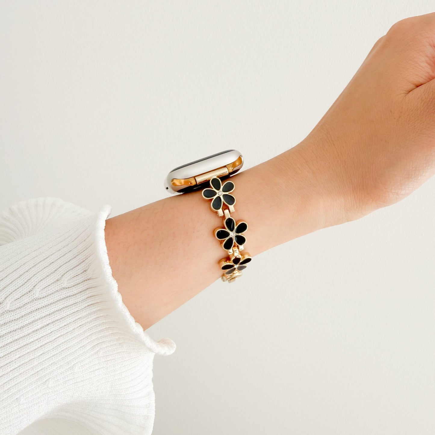 Bracelet with black floral charms Wrist wearing a gold watch APPLE women
