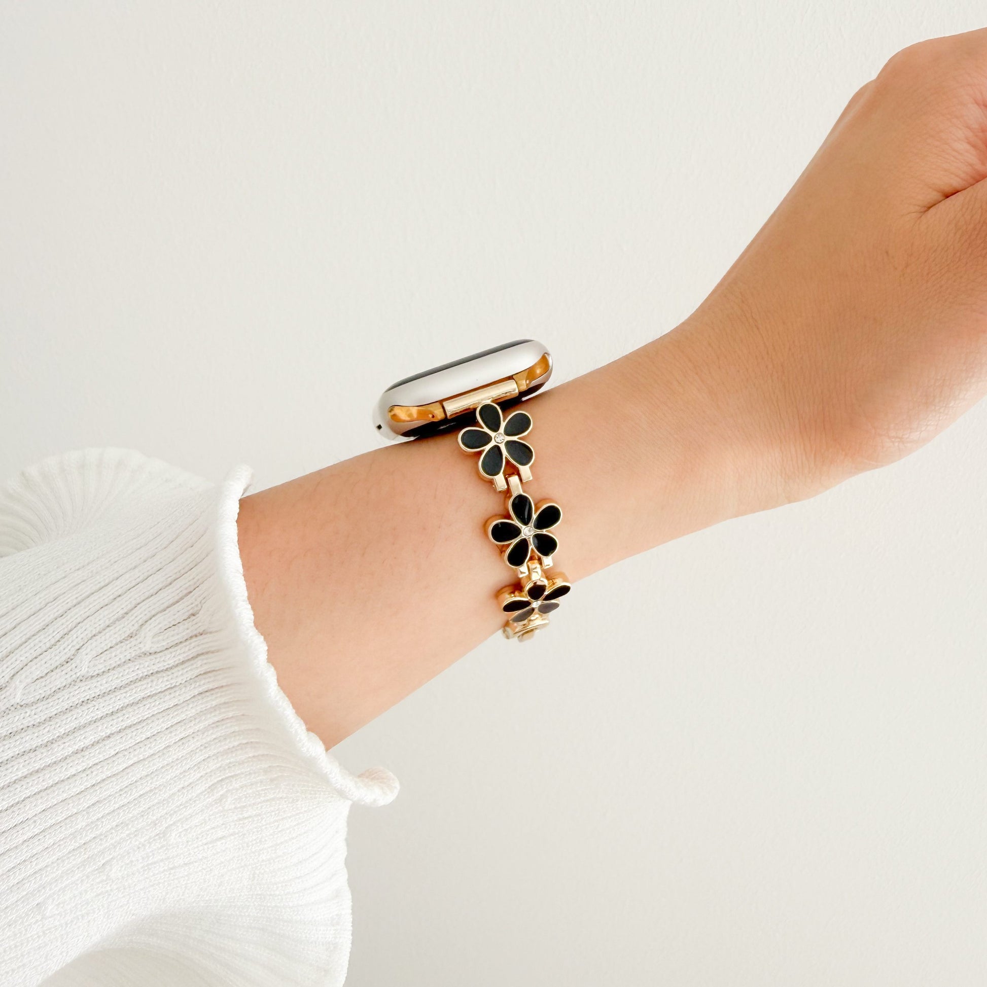 Bracelet with black floral charms Wrist wearing a gold watch APPLE women