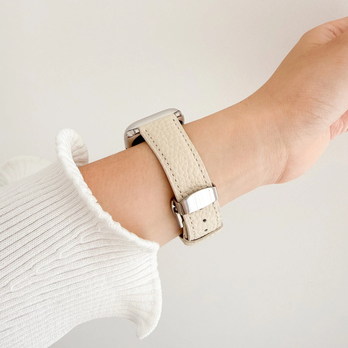 Migliara Apple Watch Band in beige leather worn on wrist with a white knit sleeve, side view