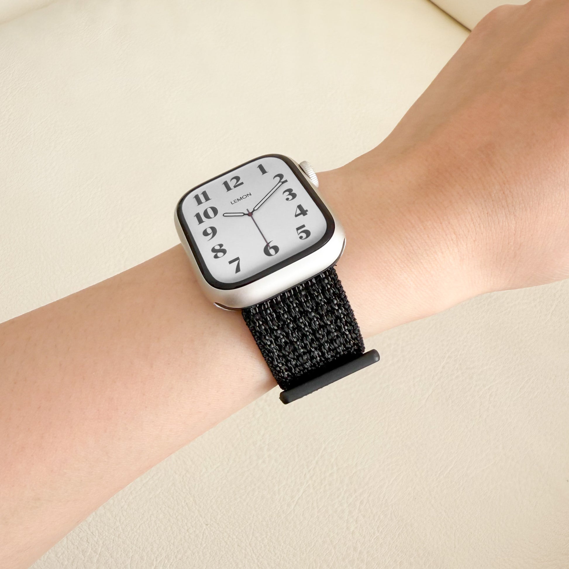 Wrist wearing a APPLE WATCH watch with a black strap on a beige background