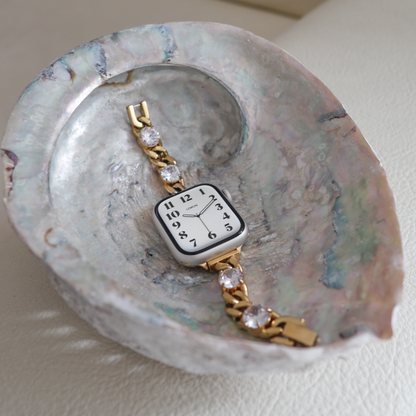 Blossom Apple Watch Band in gold stainless steel with crystals, laid in a pearly shell dish