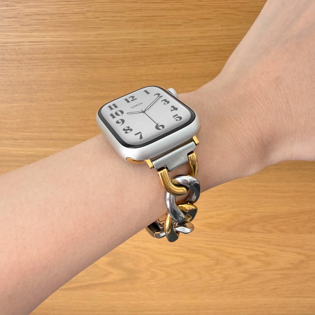 Wrist wearing a watch with a gold and silver chain strap on a wooden surface