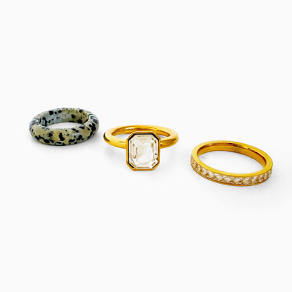 Cookies & Cream Ring Set laid out as three separate rings: speckled dalmatian jasper band, gold-tone ring with an emerald-cut clear rhinestone, and gold-tone rhinestone row band