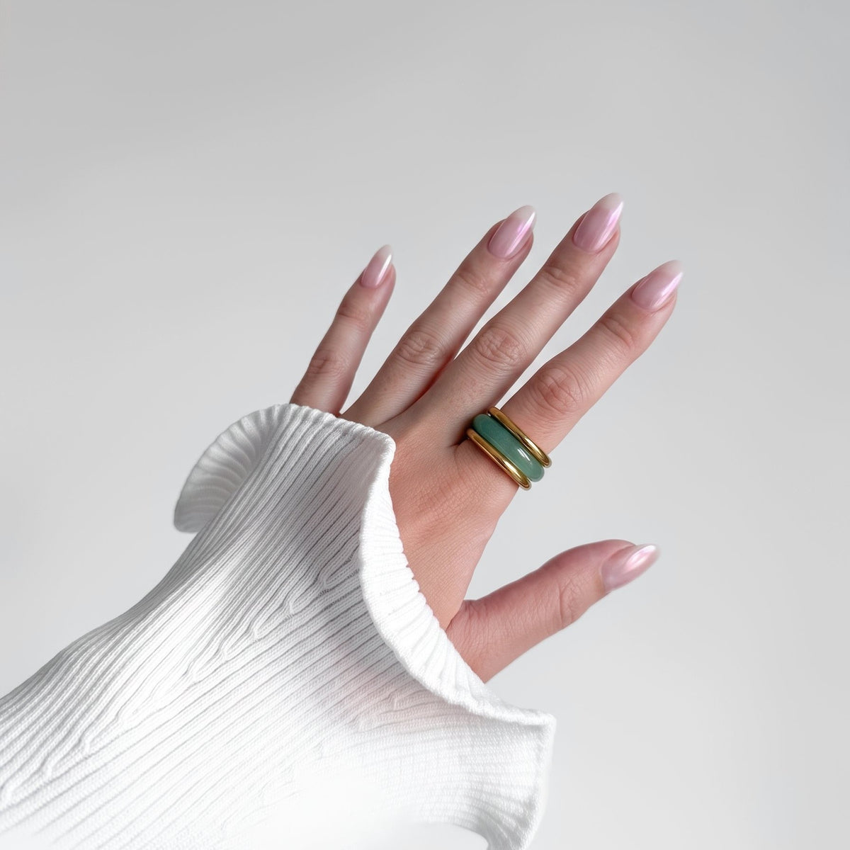 Matcha Ring Set worn on a woman's hand, green stone band between two gold-tone rings, white ribbed knit sleeve