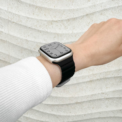 Magnetic Snap Silicone Apple Watch Band in black and grey worn on wrist with a white knit sleeve, watch face view