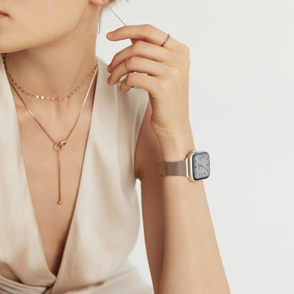 Woman wearing the Slim Milanese Apple Watch Band in rose gold, wrist raised near her chest in a cream top